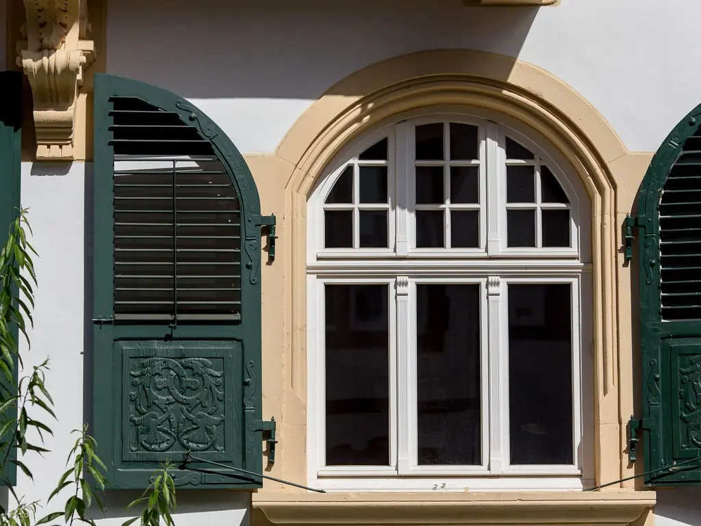 Restauriertes historisches Rundbogenfenster mit grünen Fensterläden